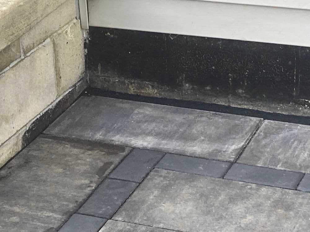 Corner of a patio with patterned gray paving stones and a black wall detail.