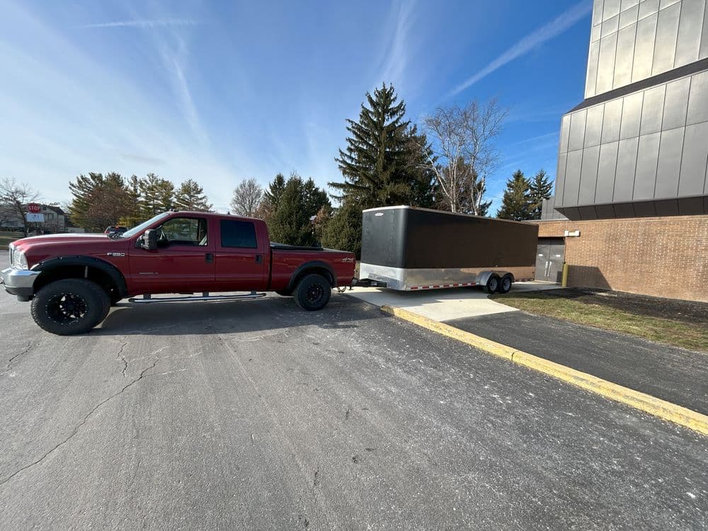 Red pickup truck towing a black trailer beside a commercial building on a sunny day.