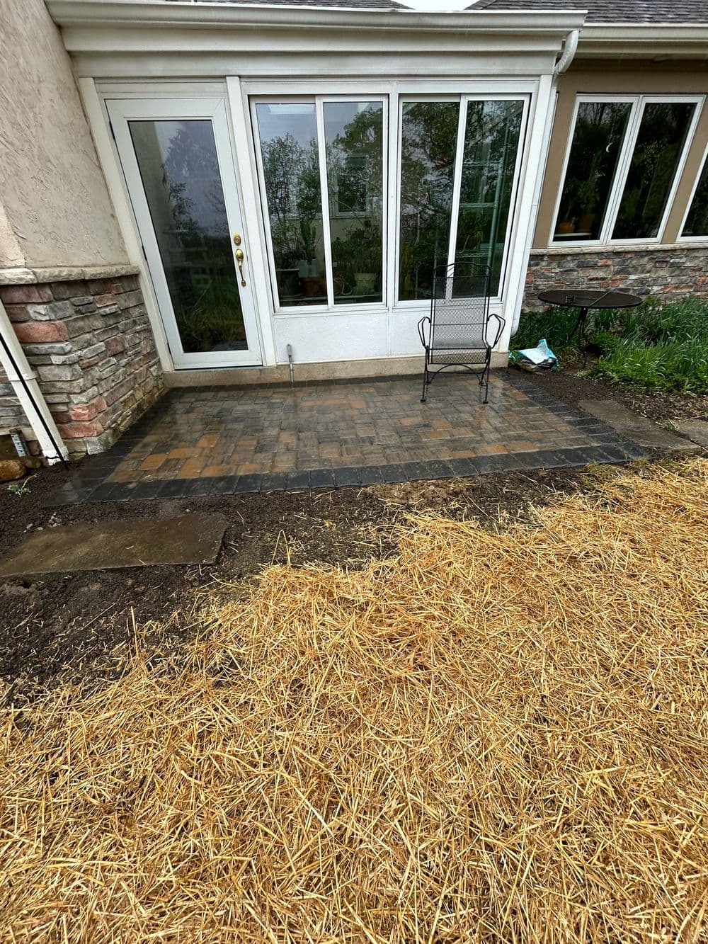 Paved patio area with a chair beside a house, featuring natural stone elements and straw ground.