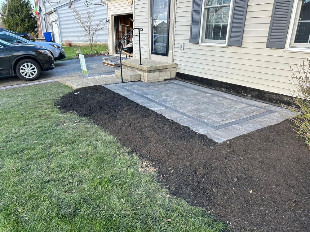 Newly installed paver patio with landscaping around residential entrance, featuring fresh mulch.