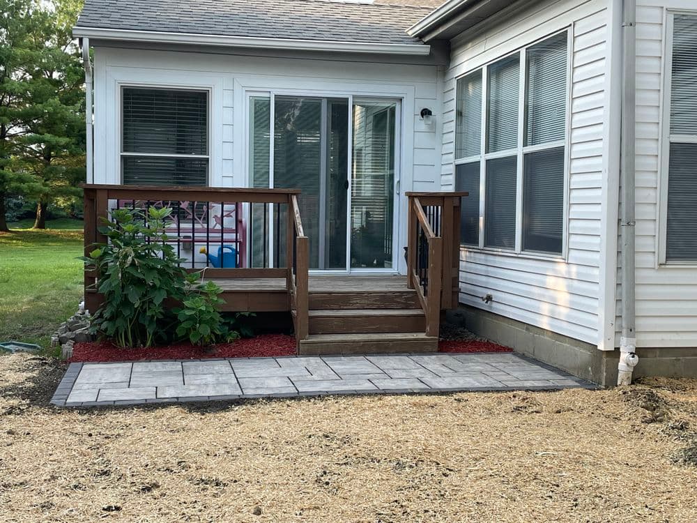 Patio with a wooden deck and stairs, surrounded by landscaping and gravel.