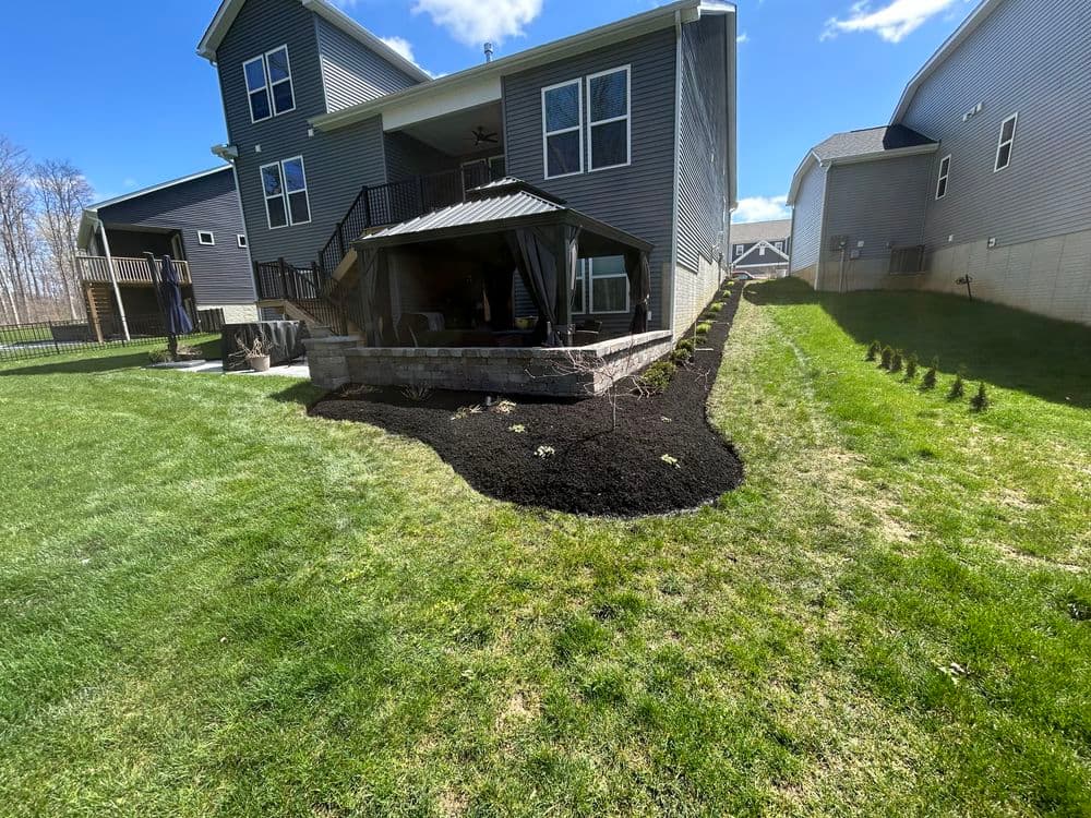 Backyard landscape featuring freshly mulched garden beds and a patio area behind a two-story home.