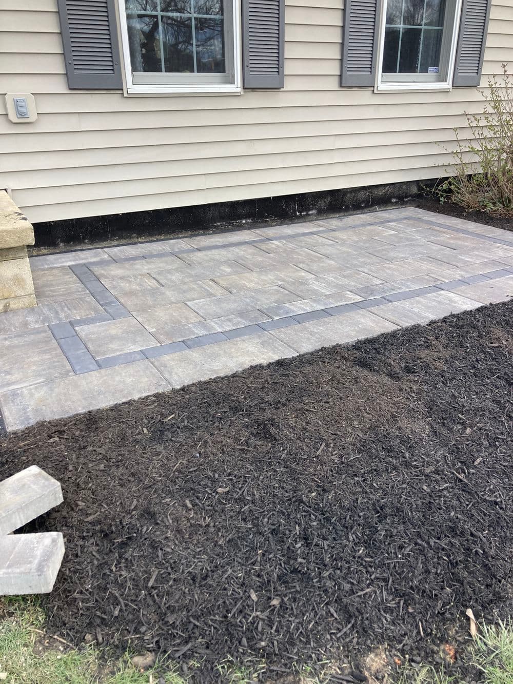 Newly installed paver patio with decorative border and freshly laid mulch.