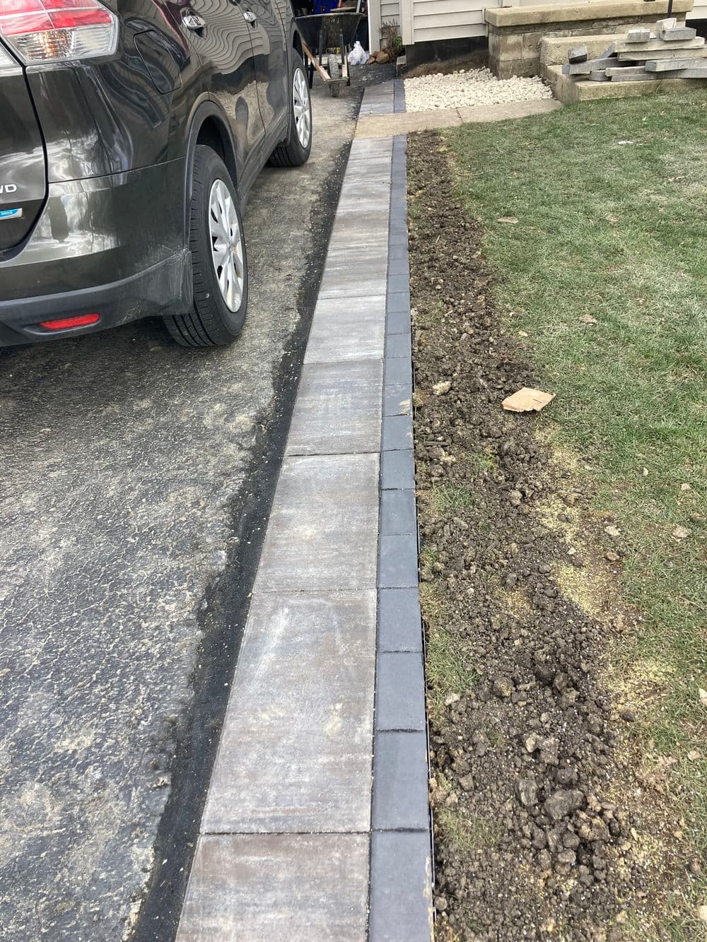 Paved driveway border alongside grass and gravel area with parked car.