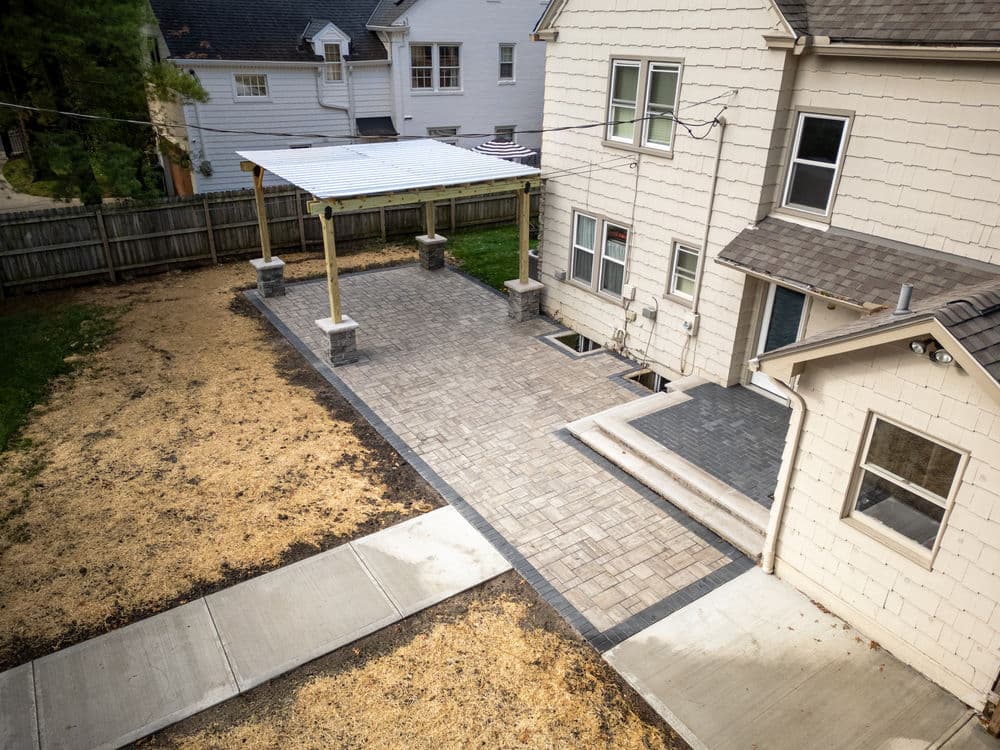 Aerial view of a backyard with a paved patio, pergola, and newly landscaped areas.