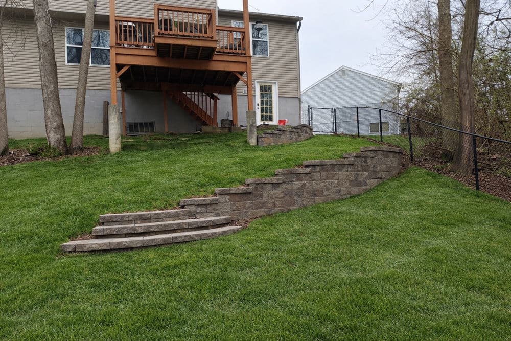 Landscape design featuring stone steps leading to a wooden deck in a backyard. Green lawn.