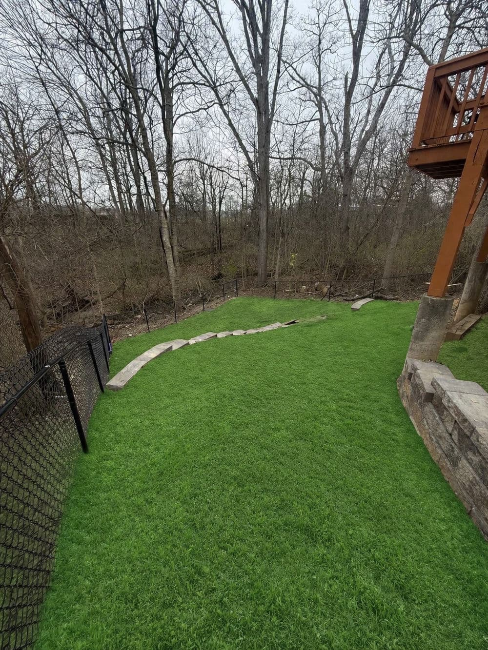 Lush artificial grass lawn with stone pathway and wooded area in the background.