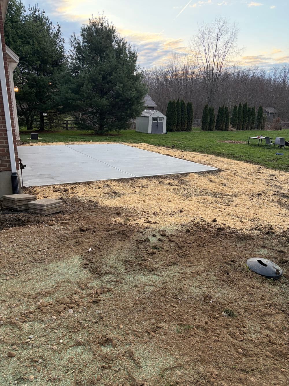 Concrete patio installation in a backyard with freshly prepared soil and greenery.