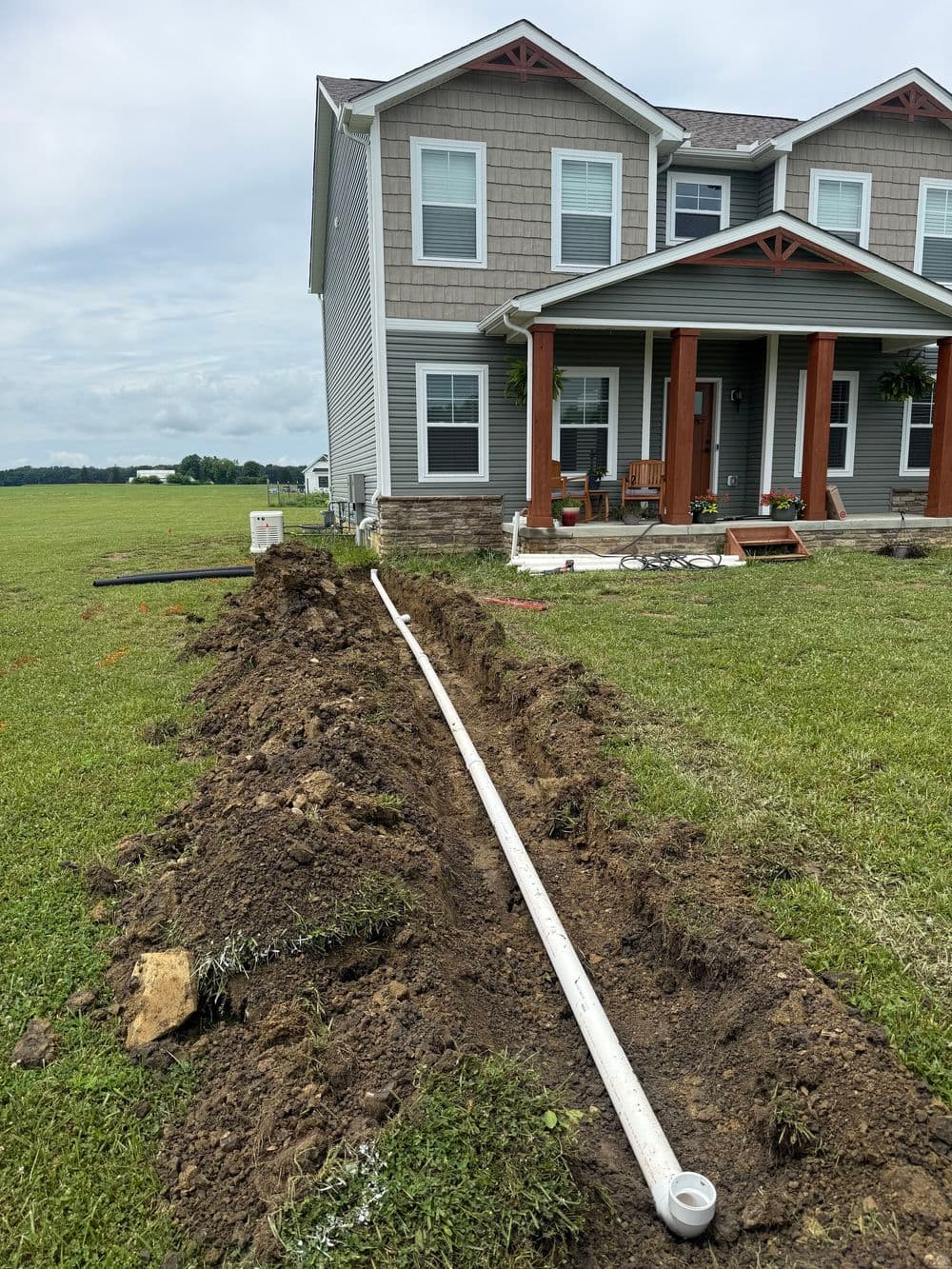 Trenched yard with white drainage pipe near a modern house and lawn.