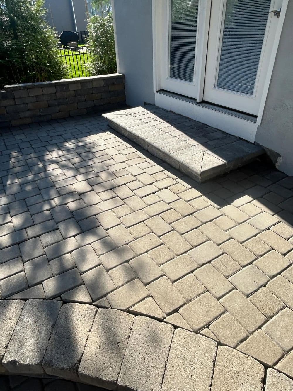 Paved patio featuring a step and retaining wall near a house entrance.