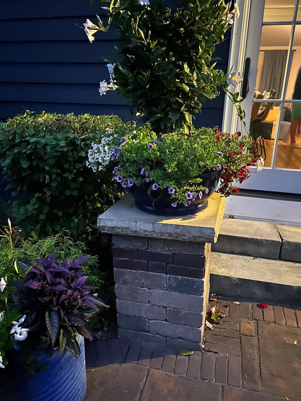 Colorful potted flowers on a stone pedestal by a house entrance at dusk.