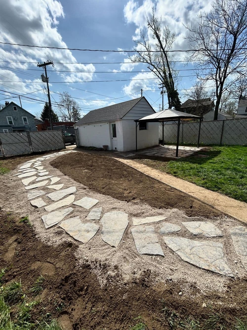 Backyard landscape featuring a stone pathway leading to a shed and green grass under a cloudy sky.